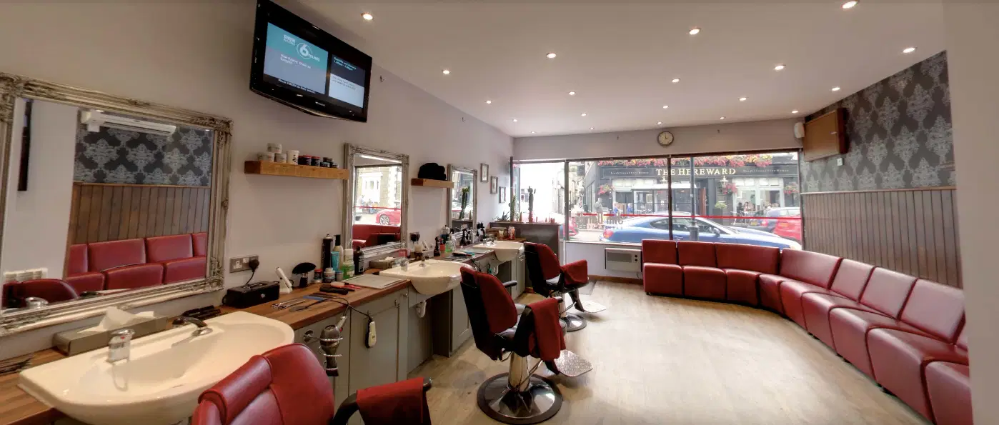 Wide-angle view of Jim Dandy Barber Shop with three barber stations, mirrors, red leather chairs, and large front windows
